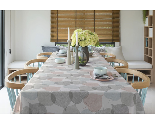 Gedeckter Esstisch mit Tischdecke mit Blattmuster, Geschirr und Dekorationen in einem hellen Esszimmer.