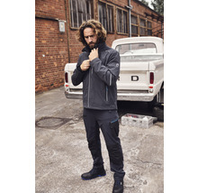 Mann in Arbeitskleidung mit Jacke, Hose und Sicherheitsschuhen vor einem Pickup.