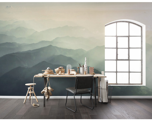 Ein Zimmer mit einer Fototapete, die eine Berglandschaft darstellt, einem Schreibtisch, einem Stuhl und einem Fenster.