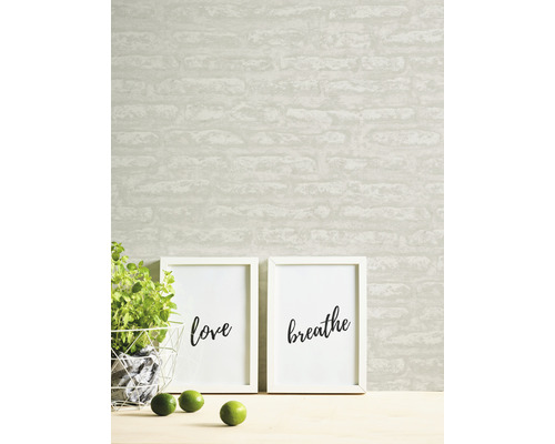 Tapete mit Backsteinmuster, zwei gerahmte Kunstdrucke mit den Worten Liebe und Atmen, Topfpflanze und Limetten auf einem Tisch.