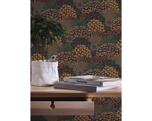Detailaufnahme eines Raumes mit einer floral gemusterten Tapete, einem Holztisch, Büchern und einer Pflanze