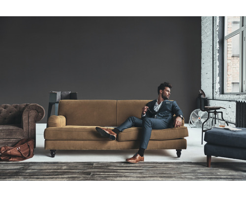 Wohnzimmer-Szene mit Sofa, Sessel, Hocker und stilvoll gekleidetem Mann