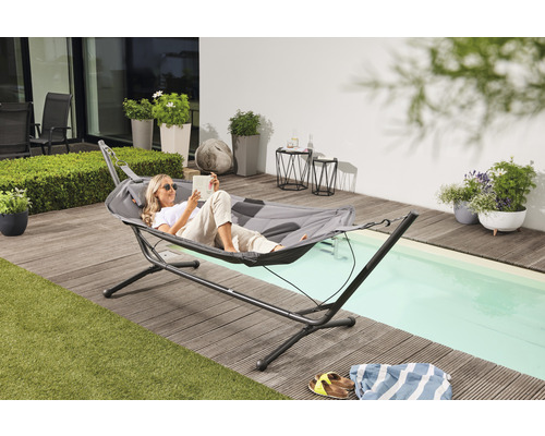 Frau liest in einer grauen Hängematte mit Gestell auf einer Terrasse