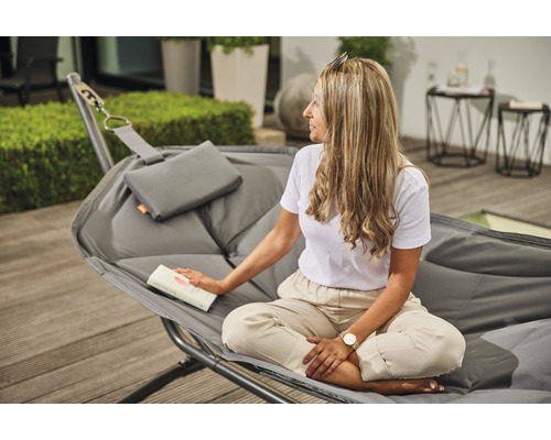 Frau liest in einer grauen Hängematte mit Kissen auf einer Terrasse