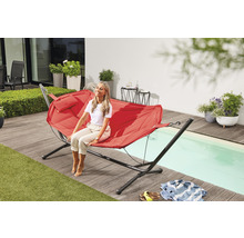 Frau entspannt sich auf einer roten Hängematte im Garten neben dem Pool