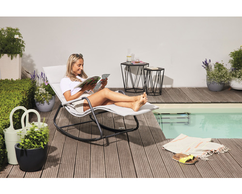 Frau liest auf einer Schaukel-Sonnenliege neben einem Pool auf einer Holzterrasse, mit Beistelltischen und Pflanzen