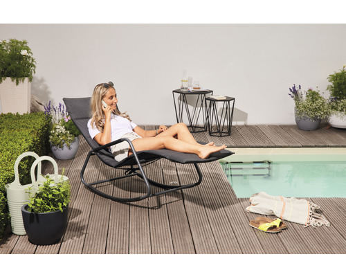 Frau entspannt sich auf einer Gartenliege neben dem Pool und telefoniert.