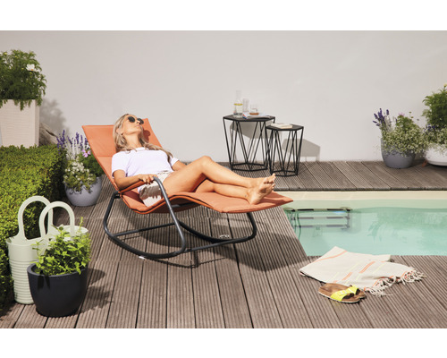 Szene mit Frau auf einer Sonnenliege neben einem Pool, Beistelltischen und Topfpflanzen auf einer Holzterrasse.