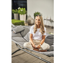 Frau sitzt auf grauer Doppelliege im Freien