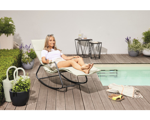 Frau entspannt sich auf einer Gartenliege auf einer Terrasse am Pool, neben Pflanzgefäßen und Beistelltischen