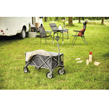 Faltbarer Bollerwagen auf einer Wiese mit Campingmöbeln und einem Wohnmobil im Hintergrund.