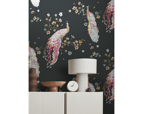 Wohnraum mit einer Tapete mit Pfauenmotiven, einer Tischlampe und dekorativen Gegenständen auf einem Sideboard.