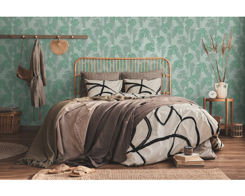 Helles Schlafzimmer mit Bett vor einer grünen Tapete mit Blättern