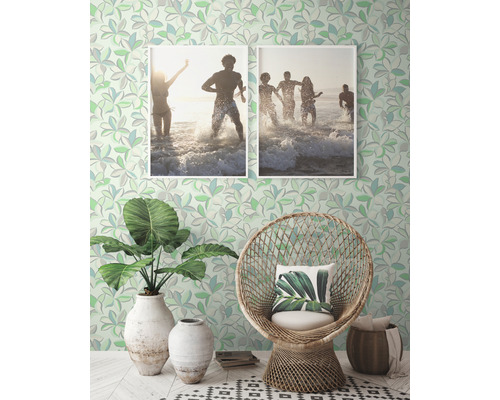 Dekoratives Zimmer mit gemusterter Tapete, Rattan-Sessel, Pflanzen und gerahmten Fotos.