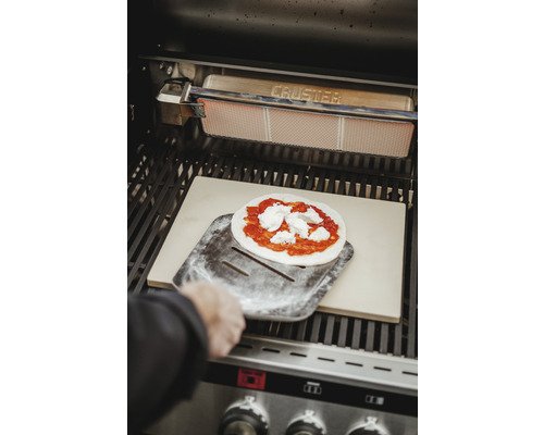 Pizza auf einem Pizzaschieber im Grill mit Pizzastein