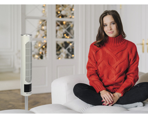 Frau sitzt neben einem Turmventilator in einem hellen Raum