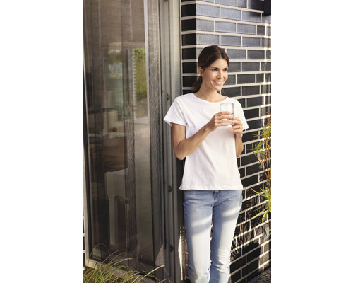 Frau steht an einer Fliegengittertür und hält ein Glas Wasser