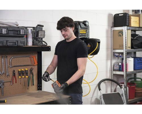 Mann reinigt einen Filter mit Druckluft in einer Werkstatt mit Werkzeugen und einem Druckluftschlauchaufroller