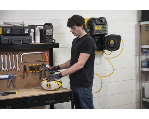 Mann pumpt einen Rugbyball mit einem Kompressor in einer Werkstatt auf.