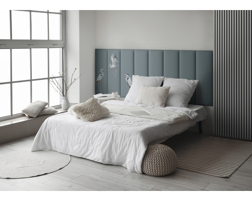 Helles Schlafzimmer mit Bett, Kissen und blauer Kopfstütze mit Vogelmotiv