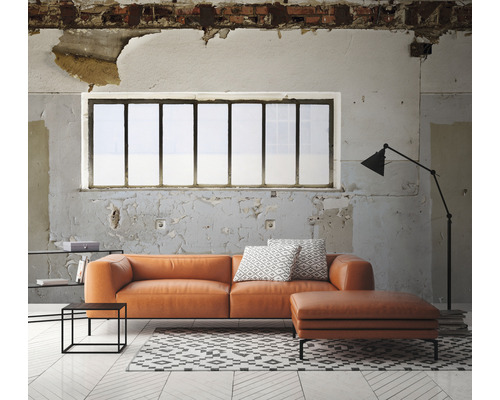 Wohnzimmer mit orangefarbenem Ledersofa, Ottomanen, Teppich und Stehlampe vor einem Fenster