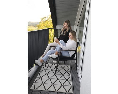 Zwei Frauen sitzen auf einem Balkon mit einem geometrischen Teppich.