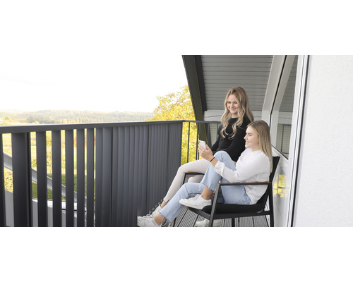 Zwei junge Frauen sitzen auf einem Balkon mit Metallgeländer und genießen die Aussicht