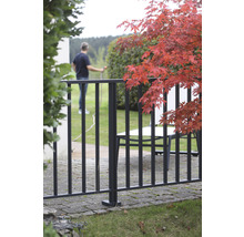 Gartenansicht mit Zaun, Gartenmöbeln und einer Person, die mit einem Gartenschlauch gießt.
