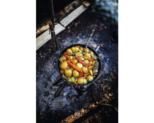 Ein Topf mit Gemüse hängt über einem Lagerfeuer.