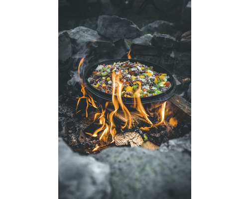 Ein Topf mit Essen steht über einem Lagerfeuer, umgeben von Steinen.