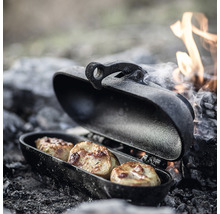 Offene Camping-Grillpfanne mit drei Kartoffeln am Lagerfeuer.