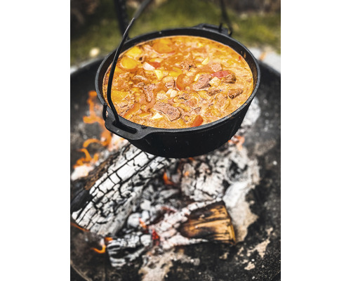 Schwarzer Dutch Oven über einem Lagerfeuer mit Essen gefüllt.