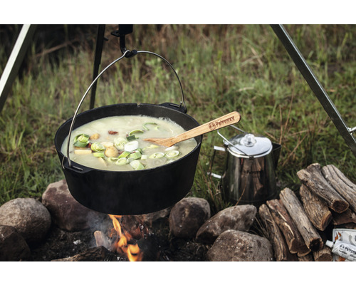 Gusseisen Topf über offenem Feuer mit Suppe und Holzlöffel, Campingkocher im Hintergrund