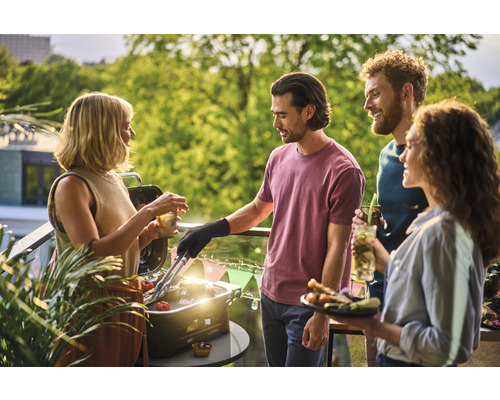 Gruppe von Freunden grillt auf dem Balkon mit einem Tischgrill und genießt die Zeit.