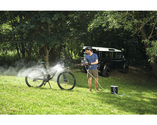 Ein Mann reinigt ein Fahrrad mit einem mobilen Hochdruckreiniger im Freien.