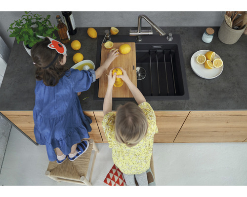 Zwei Kinder bereiten in einer Küche mit Spüle auf einer Holzplatte Zitronensaft zu.