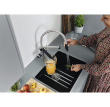 Frau wäscht Kräuter unter einem Wasserhahn in einer modernen Küche.