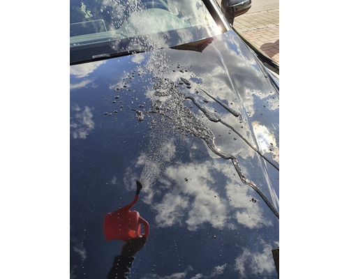 Wasser wird mit einer Gießkanne über ein Auto gegossen, wodurch ein Abperleffekt entsteht