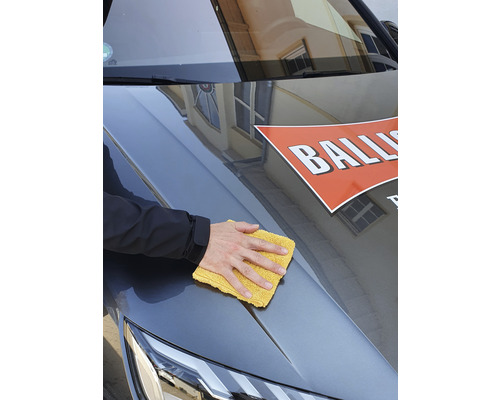 Eine Person reinigt ein Auto mit einem gelben Mikrofasertuch.