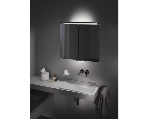 Modernes Badezimmer mit beleuchtetem Spiegelschrank, Waschbecken und Accessoires.