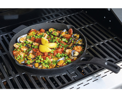 Paella in einer Bratpfanne auf einem Grill zubereitet.