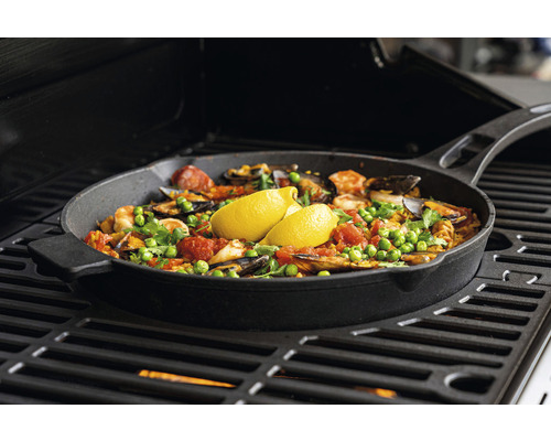 Paella in einer Eisenpfanne auf einem Grill zubereitet