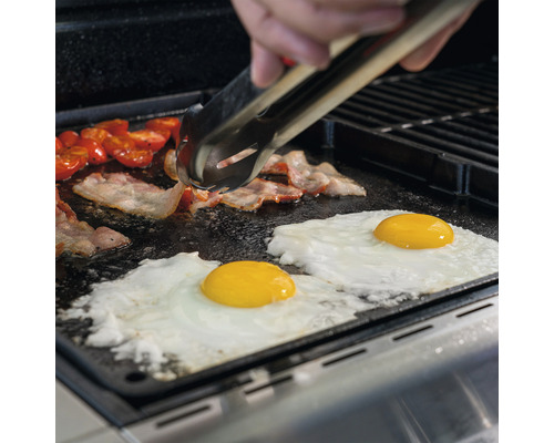 Speck, Eier und Tomaten werden auf einer Grillplatte mit einer Grillzange zubereitet.