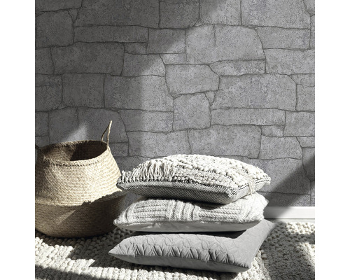 Wand mit Steinmuster, Korb und Kissen auf einem Teppich.