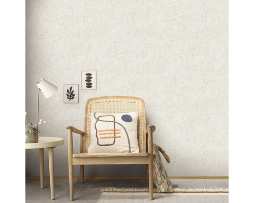 Raumansicht mit Raufasertapete, einem Stuhl mit Kissen, einem Tisch und dekorativen Bildern an der Wand.