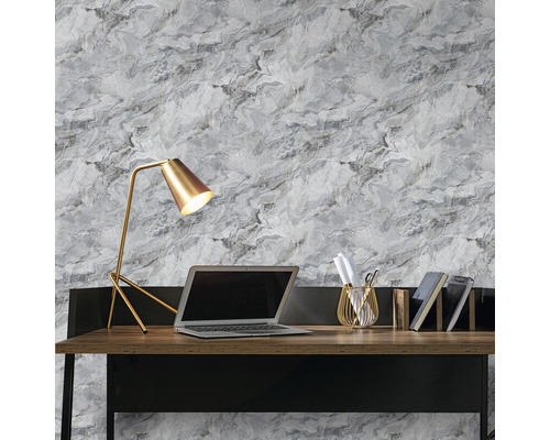 Schreibtisch mit Lampe, Laptop, Stifthalter und Büchern vor einer Wand mit Marmortapete