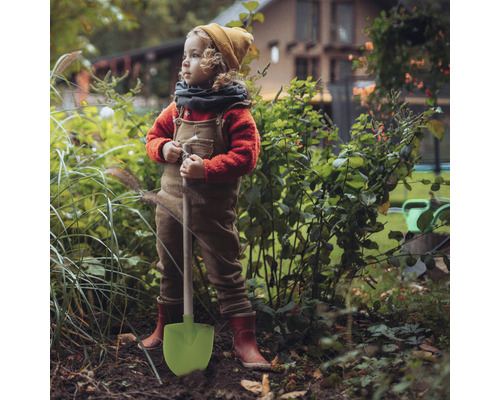 Ein Kind mit einer Schaufel steht im Garten.