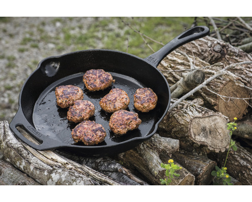Gusseisenpfanne mit Bratlingen auf Holzstapel