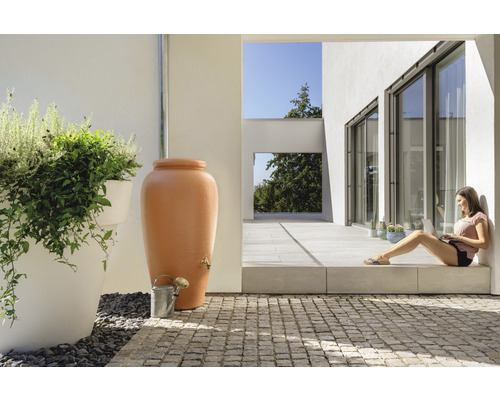 Szene mit Regenwassertonne, Gießkanne und Frau mit Laptop auf der Terrasse