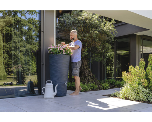 Mann bepflanzt Regenspeicher mit Blumen in einem Garten